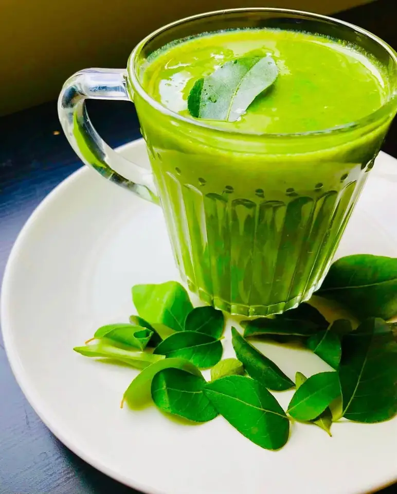 A glass of green kola kanda with leaves on a white saucer
